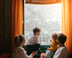 A man, a woman and two young boys look out a window at the snow.