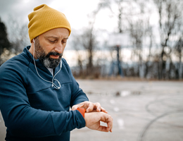 A runner wearing earbuds looks at a watch-like device.